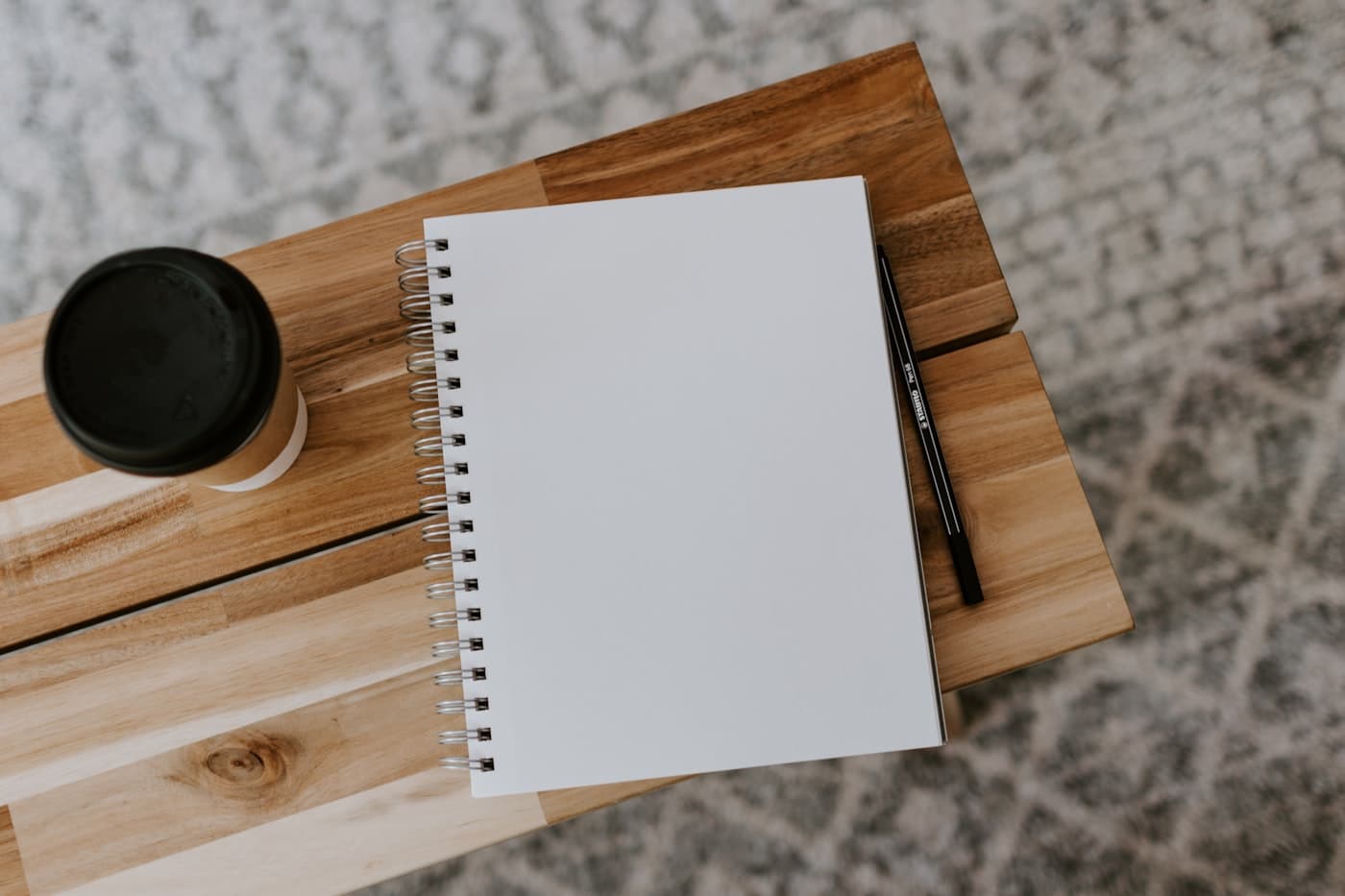 A blank spiral notebook and a coffee cup on a light wooden bench
