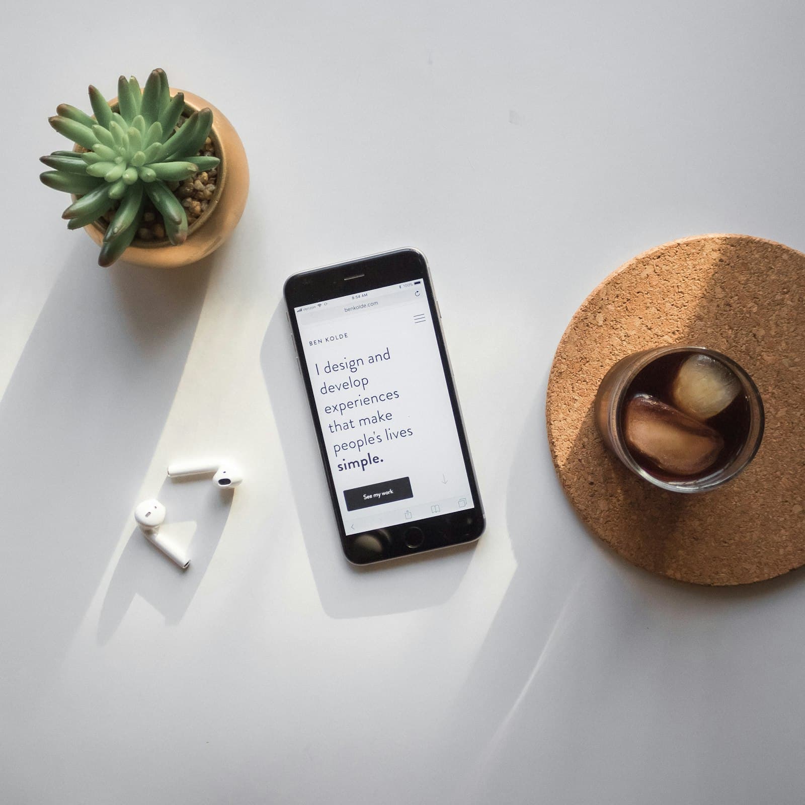 A phone showing a web page on a white desk beside earphones, a plant and a glass