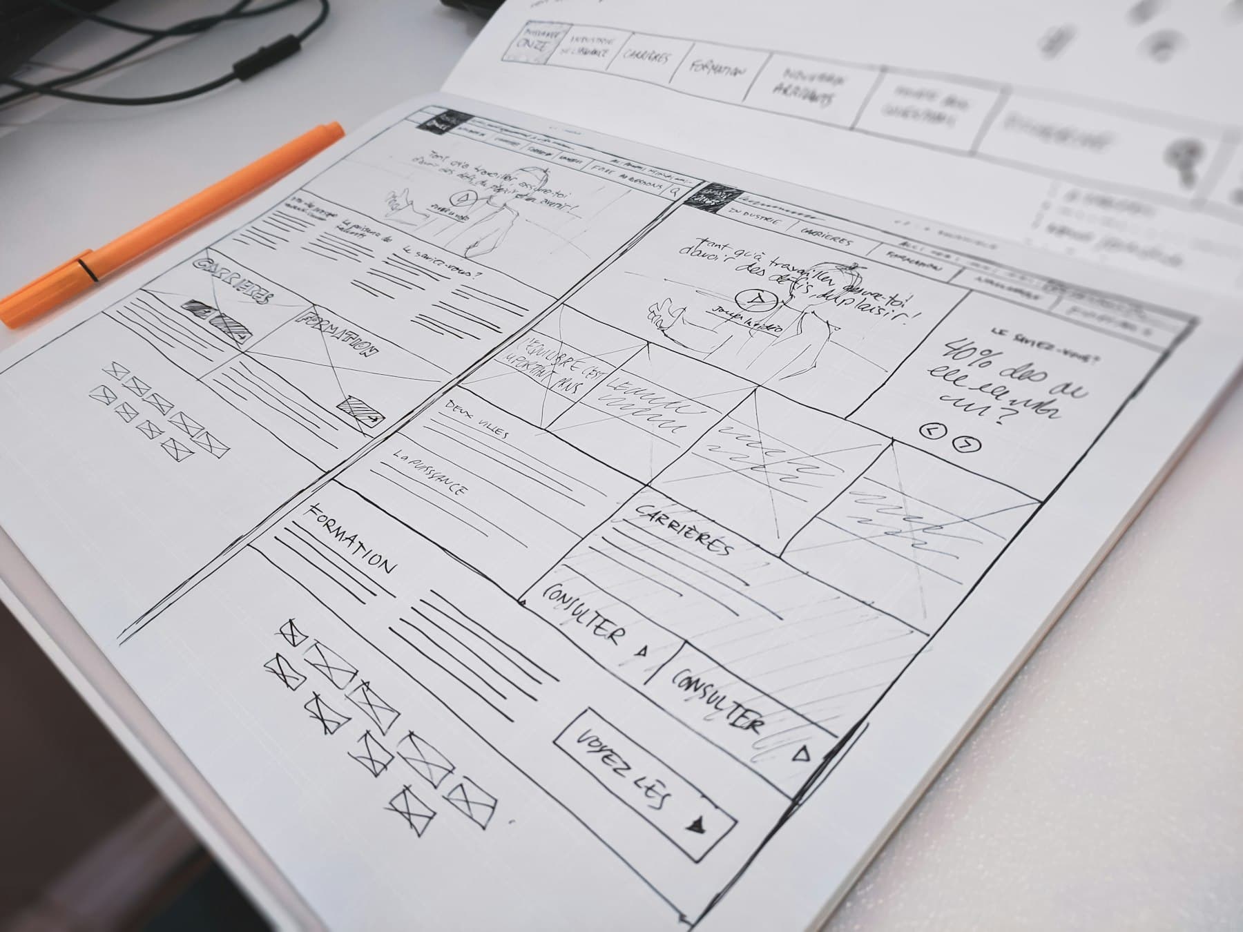A hand-drawn page wireframe on paper next to an orange pen