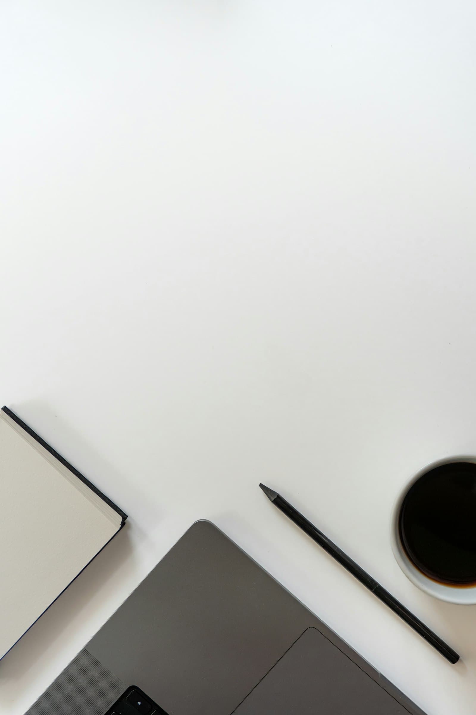 A pale desk seen from above with a notebook, pencil and cup of coffee